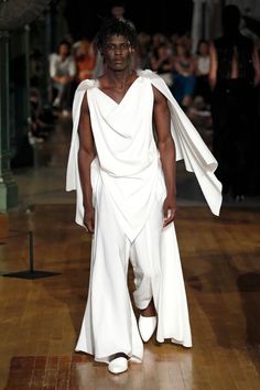 a man in a white outfit walking down a runway