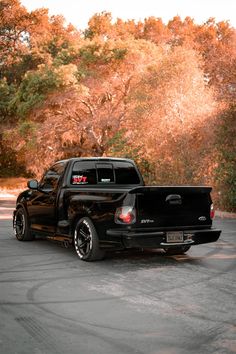 a black pick up truck parked in a parking lot next to trees with orange leaves