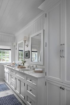 a large bathroom with two sinks and mirrors on the wall, along with white cabinets