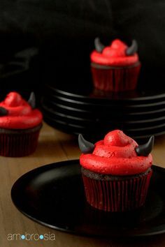 cupcakes with red frosting and horns on them are sitting on black plates