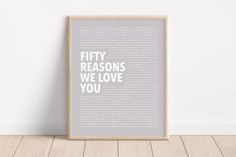 a framed poster with the words fifty reasons we love you in white on a wooden floor