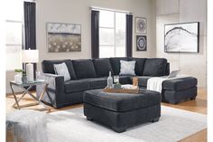 a living room with gray furniture and white rugs on the hardwood floor, along with two large windows