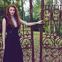 a woman standing in front of an iron gate with her hand on the door handle