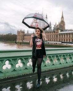 a woman holding an umbrella over her head while standing on a bridge in front of the big ben clock tower