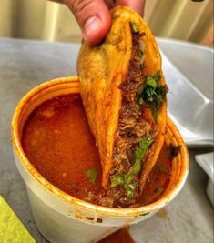 a hand holding a piece of food over a bowl filled with chili and other foods