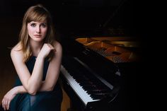 a woman sitting in front of a black piano with her arms on her chest and looking at the camera