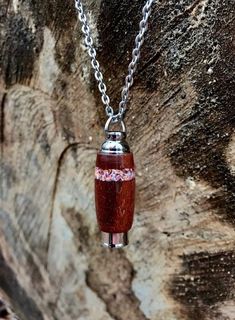 a necklace with a bottle on it hanging from a chain that is attached to a rock