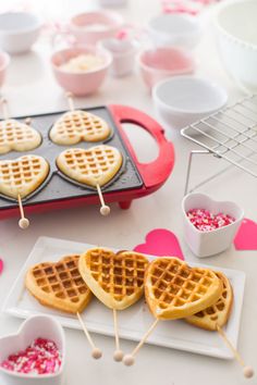 heart shaped waffles with toothpicks in them on a white plate next to other food items