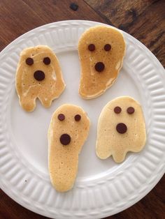 three pancakes with chocolate chips in the shape of ghost faces on a white paper plate