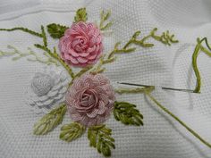 two pink roses are being worked on with crochet hooks and thread as part of an embroidery project