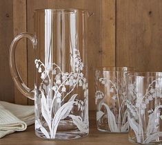 three clear glass pitchers and two glasses on a wooden table next to a cloth napkin