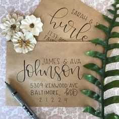 the wedding stationery is laid out on top of a piece of brown paper with white flowers