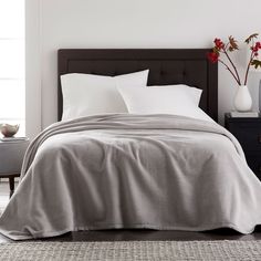 a bed with white sheets and pillows in a room next to a table with vases on it