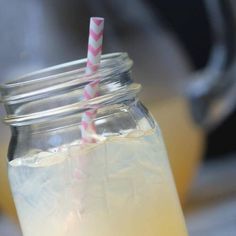 a mason jar filled with liquid and two pink striped straws next to a teapot