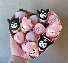 a person holding a heart shaped box filled with cupcakes and decorated chocolates