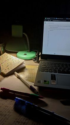 an open laptop computer sitting on top of a desk next to a notebook and pen