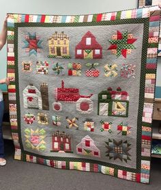 a woman standing next to a quilted wall hanging