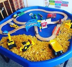 a toy train set in a blue plastic container with yellow toys on the tracks and construction vehicles