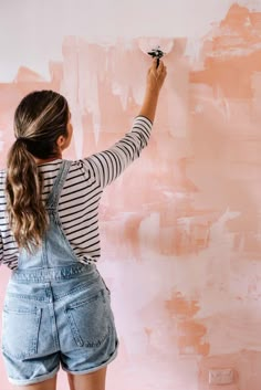 a woman is painting a wall with pink and white paint in the background, she has her back to the camera