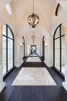 an elegant hallway with arched windows and chandelier hanging from the ceiling, along with hardwood flooring