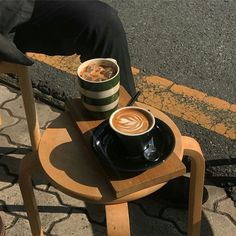 a cup of coffee sitting on top of a wooden table next to a person's legs