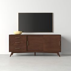 a large tv mounted on top of a wooden cabinet next to a bowl and vase