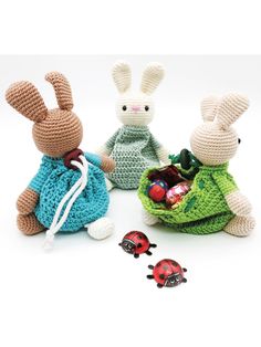 three crocheted rabbits sitting next to each other with candy in their hands and ladybugs on the ground