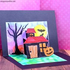 a paper cut out of a house with bats and pumpkins on the roof, next to a card that says happy halloween