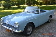 an old blue car is parked on the gravel