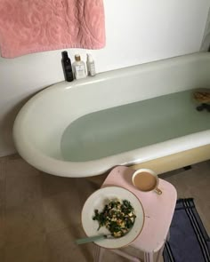 a white bath tub sitting next to a pink towel on top of a wooden table