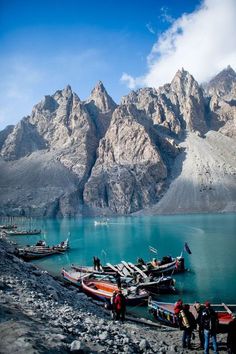 several boats are docked at the shore of a mountain lake with mountains in the background