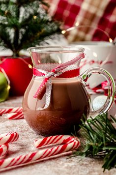 a glass mug filled with hot chocolate on top of a table next to candy canes