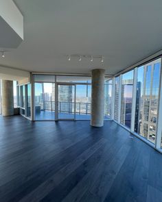 an empty room with wooden floors and large windows looking out onto the cityscape