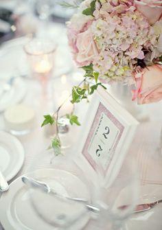 the table is set with white plates and silverware, pink flowers, and candles