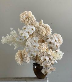 a vase filled with lots of white flowers on top of a wooden table next to a wall