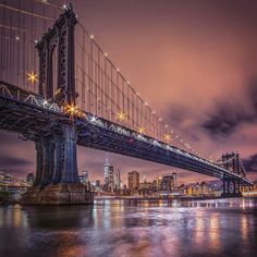 the manhattan bridge is lit up at night with lights reflecting off it's sides