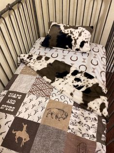 a baby crib with a cow print blanket on it's side and two pillow cases