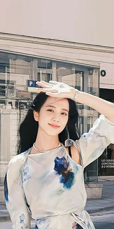 a woman standing on the street holding her hair in one hand and wearing a white shirt with blue flowers on it