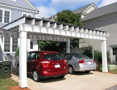 two cars parked under an attached pergolan in front of a gray house with white trim