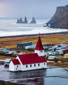 a small white church with a red roof near the ocean and cliffs in the background