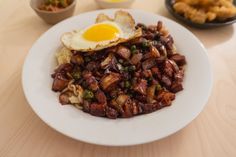 a white plate topped with meat and an egg on top of it next to other foods