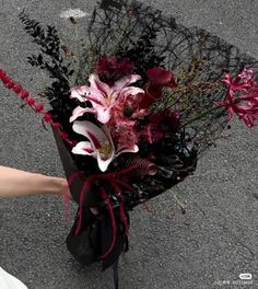 a bouquet of flowers is being held by someone's hand on the street side