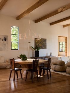 a dining room table and chairs in front of a large window with wood beams on the ceiling