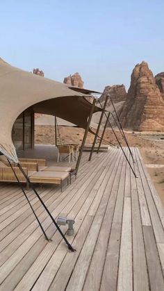 a large tent on top of a wooden deck next to mountains and sand dunes in the distance