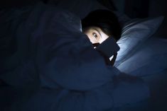 a woman laying in bed under a blanket looking up at the light coming through her eyes