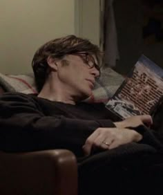 a man laying on top of a couch holding a book in his hand and reading it