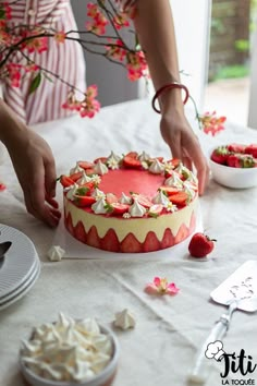 a woman is decorating a cake with strawberries and whipped cream on the table