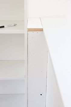 a white shelf with a pen on top of it next to an empty bookcase