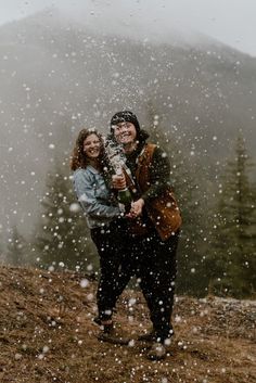 a man and woman standing in the snow holding an umbrella while it is snowing