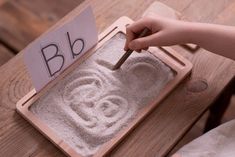 a child's hand is writing on a sand tray with a letter b in it